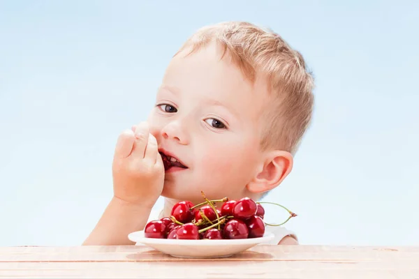 Дитина з червоними ягодами, хлопчик їсть і вибирає вишню . — стокове фото