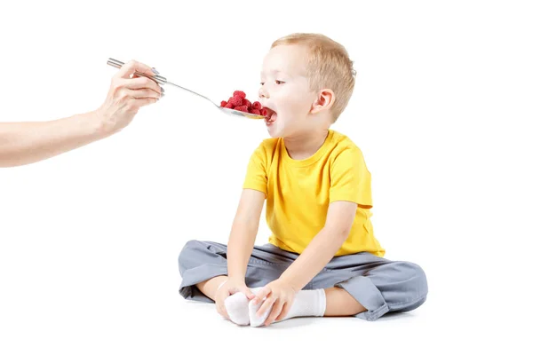 小さな男の子は白で分離されたラズベリーを食べています。 — ストック写真