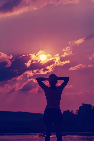 Silhouette of a young woman with arms raised in the backdrop of the setting sun — Stock Photo, Image