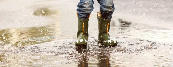 Criança com botas de chuva pula em uma poça — Fotografia de Stock