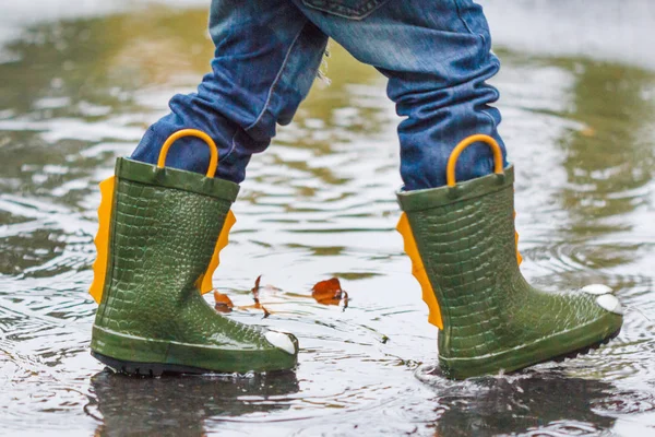 Criança com botas de chuva pula em uma poça — Fotografia de Stock
