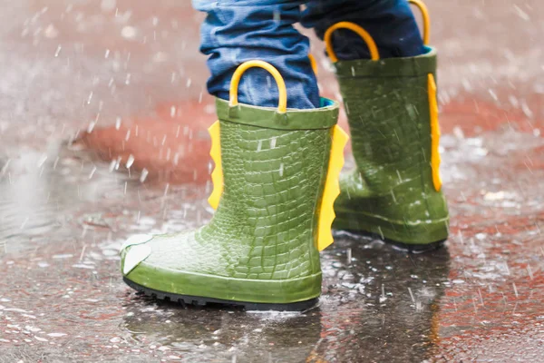 Enfant avec des bottes de pluie saute dans une flaque — Photo