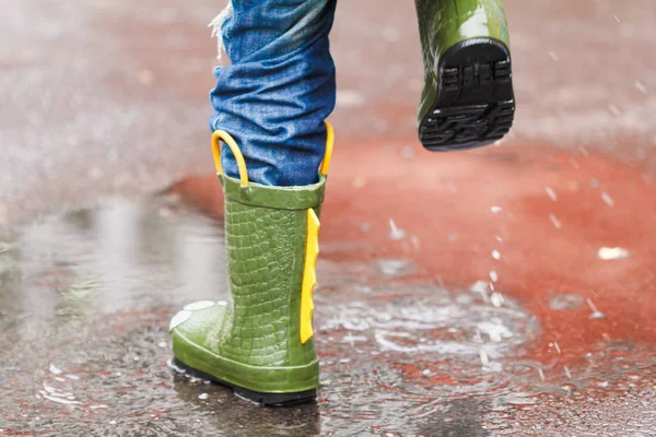 Enfant avec des bottes de pluie saute dans une flaque — Photo