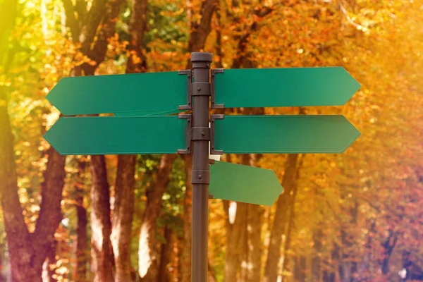 Señales de tráfico direccionales en blanco contra el follaje otoñal. Flechas de metal verde en el poste de señalización . — Foto de Stock