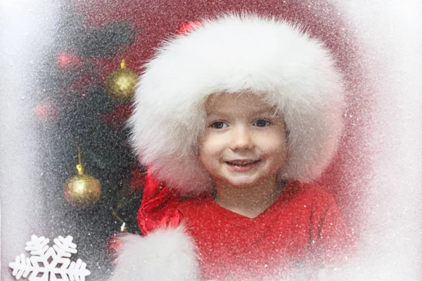 Criança em Santa cap com árvore de Natal na janela olhando para o inverno. Criança e queda de neve . — Fotografia de Stock