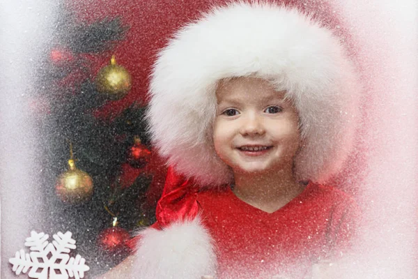 Criança em Santa cap com árvore de Natal na janela. Criança e queda de neve . — Fotografia de Stock