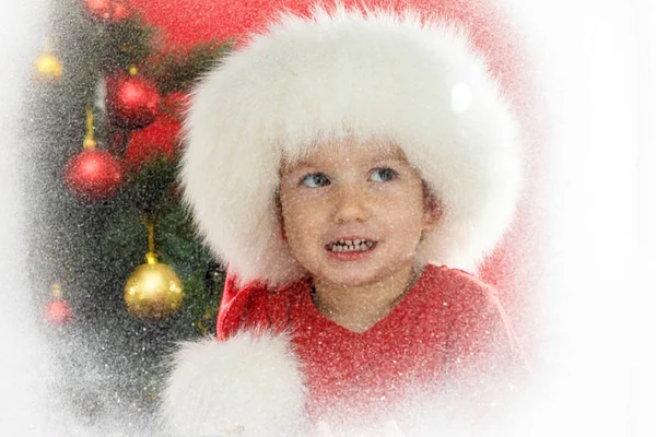 孩子在圣诞老人帽子与圣诞树在窗口。孩子和降雪. — 图库照片