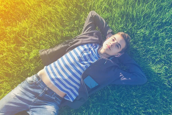 Young man lying on the grass listing music