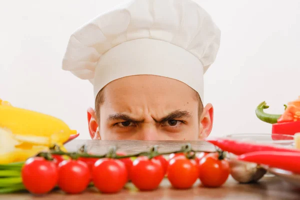 Man met kok GLB op witte achtergrond. Chef-kok met groenten op tafel. Koken met vrolijk gezicht in gezicht close-up. — Stockfoto