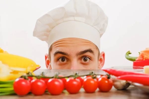Homme avec casquette de cuisson sur fond blanc. Chef avec légumes sur la table. Cuire avec le visage joyeux dans le visage de près . — Photo