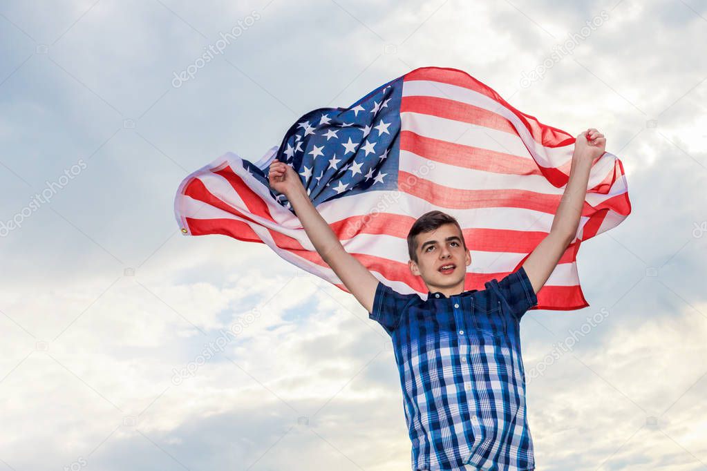 Young teenage boy holding a flag of the United States of America over shoulders