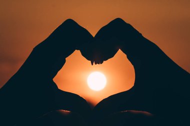 Siluet el renkli güneş gökyüzü üzerinde kalp şeklinde aşk sembolü, gün batımı