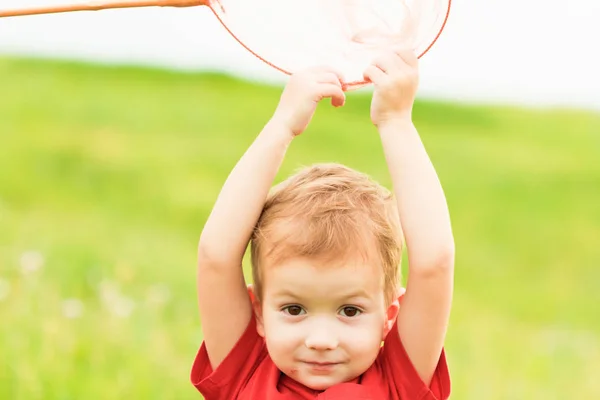 Adorable niño caucásico jugando con la cuchara-red en el prado en verano cálido y soleado o día de primavera . —  Fotos de Stock