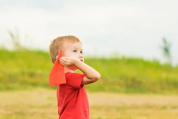 Gelukkig kind spelen met speelgoed papieren vliegtuigje tegen zomer hemel — Stockfoto
