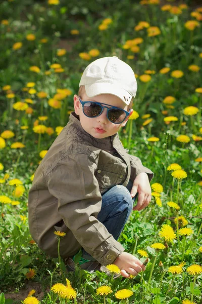 日当たりの良い夏の日にタンポポの花と緑の草の芝生の上の子。庭で遊ぶ子供. — ストック写真