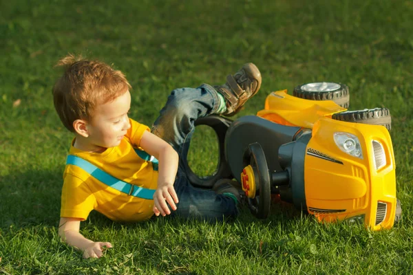 Мила позитивна дитина, що щасливо грає з дитячою машиною на зеленому лузі — стокове фото