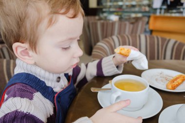 Küçük çocuk çay bardağı kurabiye ve kek ile kafede içecekler.