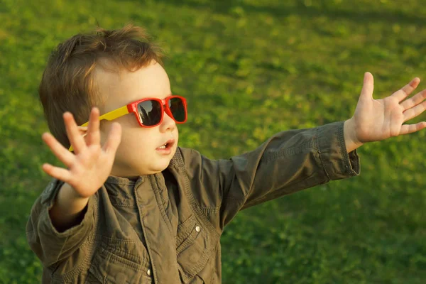 Söt rödhårig pojke i solglasögon. når ut till solnedgången. — Stockfoto