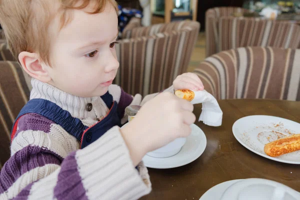 Küçük çocuk çay bardağı kurabiye ve kek ile kafede içecekler.