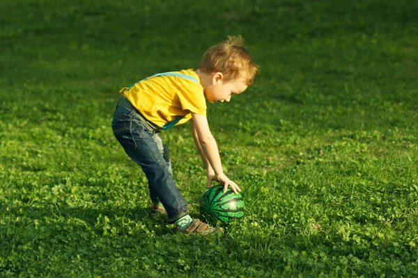 Cute positive kid, playing happily with ball on green meadow — Stock Photo, Image