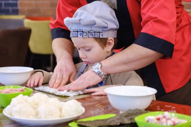Geleneksel suşi yemek alır. Çocuk aşçı olarak giyinmiş.