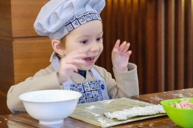 Geleneksel suşi yemek alır. Çocuk aşçı olarak giyinmiş.