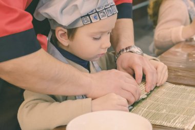 Geleneksel suşi yemek alır. Çocuk aşçı olarak giyinmiş.