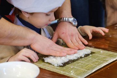Geleneksel suşi yemek alır. Çocuk aşçı olarak giyinmiş.