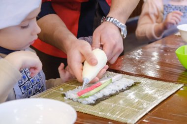 Geleneksel suşi yemek alır. Çocuk aşçı olarak giyinmiş.