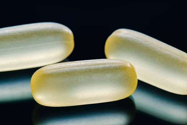 Heap of yellow capsule pills tablets medicine lying isolated on black background extreme close-up. — Stock Photo, Image