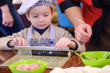 Geleneksel suşi yemek alır. Çocuk aşçı olarak giyinmiş.