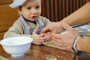 Geleneksel suşi yemek alır. Çocuk aşçı olarak giyinmiş.