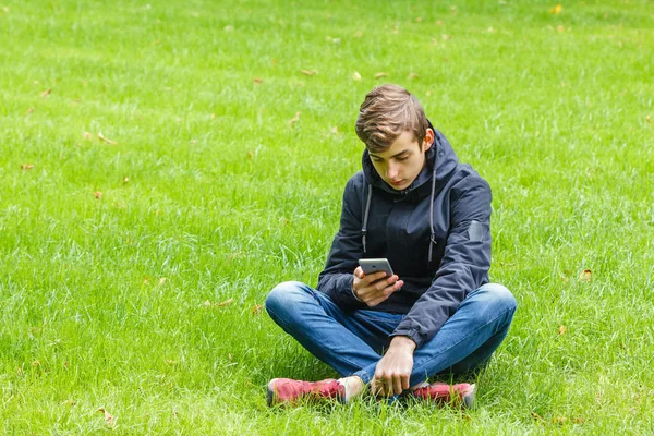 Erkek öğrenci Şehir Parkı bir çim üzerinde oturmuş bir telefonda konuşmak