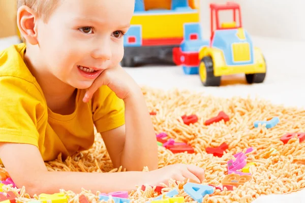 Glückliches Kind in farbigen Kleidern, das mit Plastikbuchstaben spielt. Alphabet lernen, sich auf die Schule vorbereiten. — Stockfoto