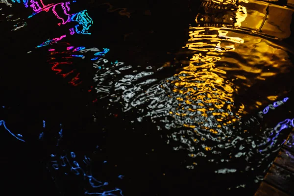 Una pozzanghera in una notte di pioggia in città con riflessi di lanterne e cartello pubblicitario nei toni del blu — Foto Stock