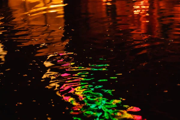 Un charco en una noche lluviosa en la ciudad con reflejos de linternas y letrero publicitario en tonos multicolores —  Fotos de Stock