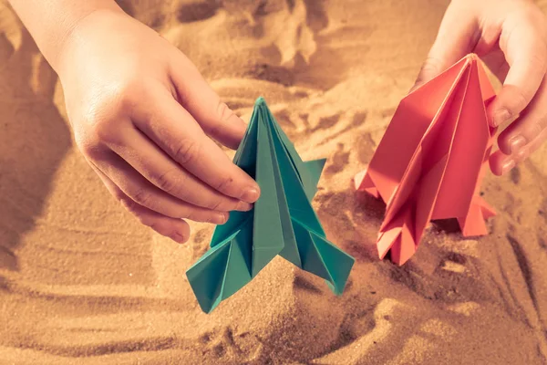 Niño feliz jugando con papel de origami hecho a mano, cohete en arena de playa, concepto de puesta en marcha —  Fotos de Stock