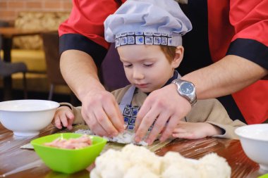 Geleneksel suşi yemek alır. Çocuk aşçı olarak giyinmiş.