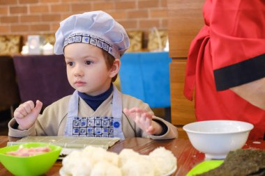 Geleneksel suşi yemek alır. Çocuk aşçı olarak giyinmiş.