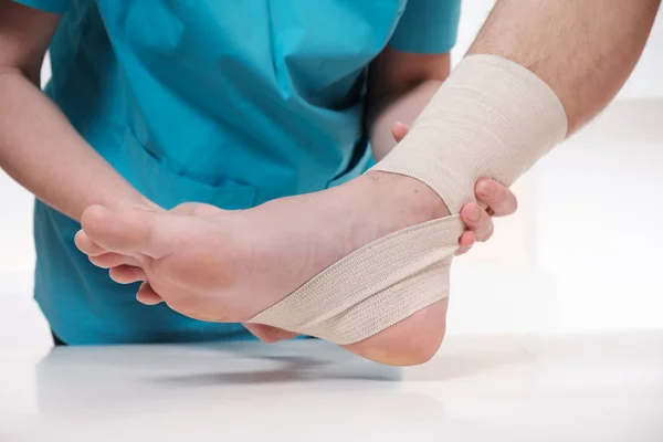 Kvinnliga läkare bandage foten av manlig patient — Stockfoto
