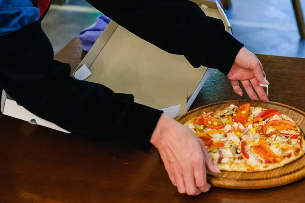 Frauenhände nehmen eine Pizza aus einer Schachtel auf dem Tisch, Draufsicht — Stockfoto