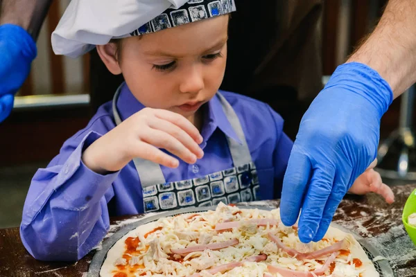 Children make pizza. Master class for children on cooking Italian food. Learn to cook a pizza kid preparing, little cook. Hands of people making pizzas together