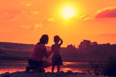 kadın ve çocuk yaz Nehri üzerinden günbatımı arka plan üzerinde.