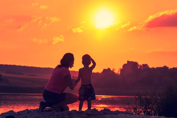 Woman and child on sunset background over summer river. — Stock Photo, Image