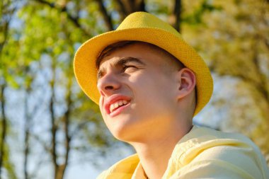 Bir portre sarı gömlek ve mavi gökyüzü, yeşil ağaç karşı şapka giymiş mutlu bir genç çocuk dışarıda,