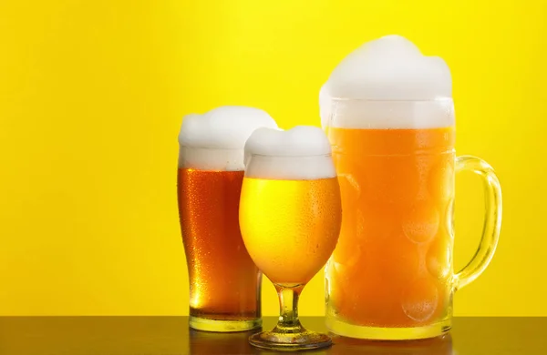 Mug and glass of beer close-up with froth over yellow background — Stock Photo, Image