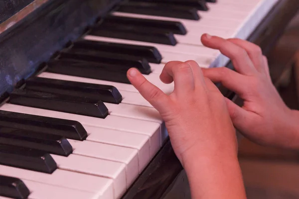 Child plays old piano with hands.