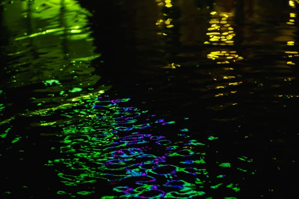 Un charco en una noche lluviosa en la ciudad con reflejos de linternas y letrero publicitario en tonos verdes —  Fotos de Stock