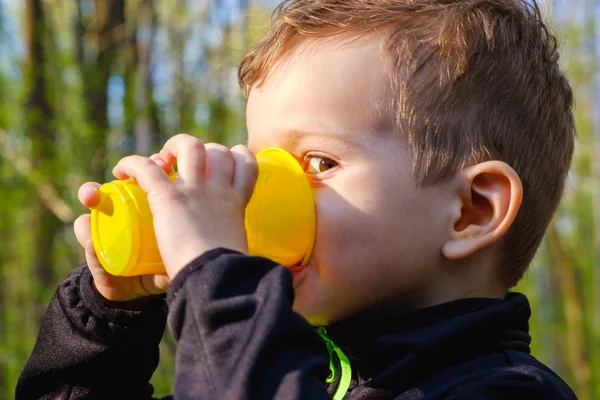 Küçük bir çocuk içecekler bir plastik bir zam cam.