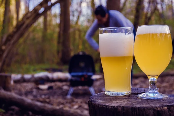 Vasos de cerveza con mujeres asando alas de pollo en la parrilla barbacoa en el fondo . —  Fotos de Stock